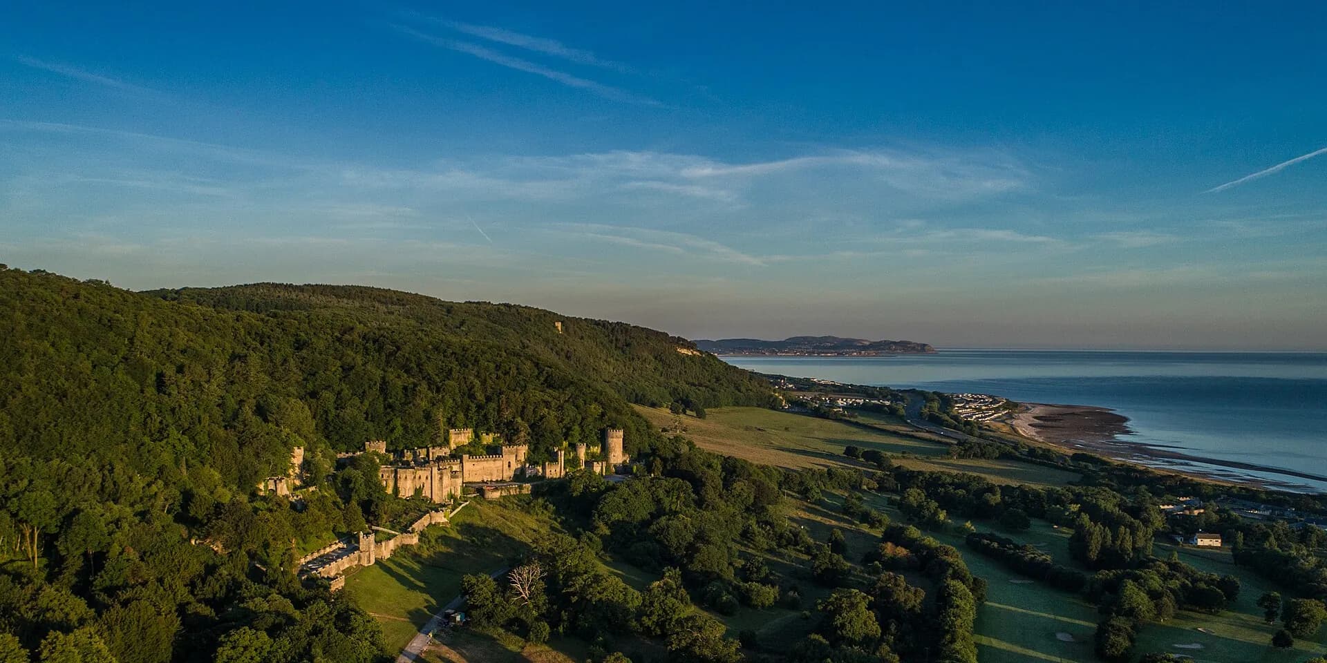 Gwrych Castle among wooded hills above Abergele, with the coast and sea stretching away, seen from the air