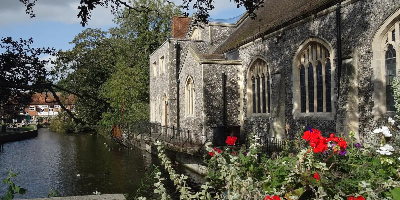 The River Anton flowing past a flint church, with red flowers on the bank in Andover