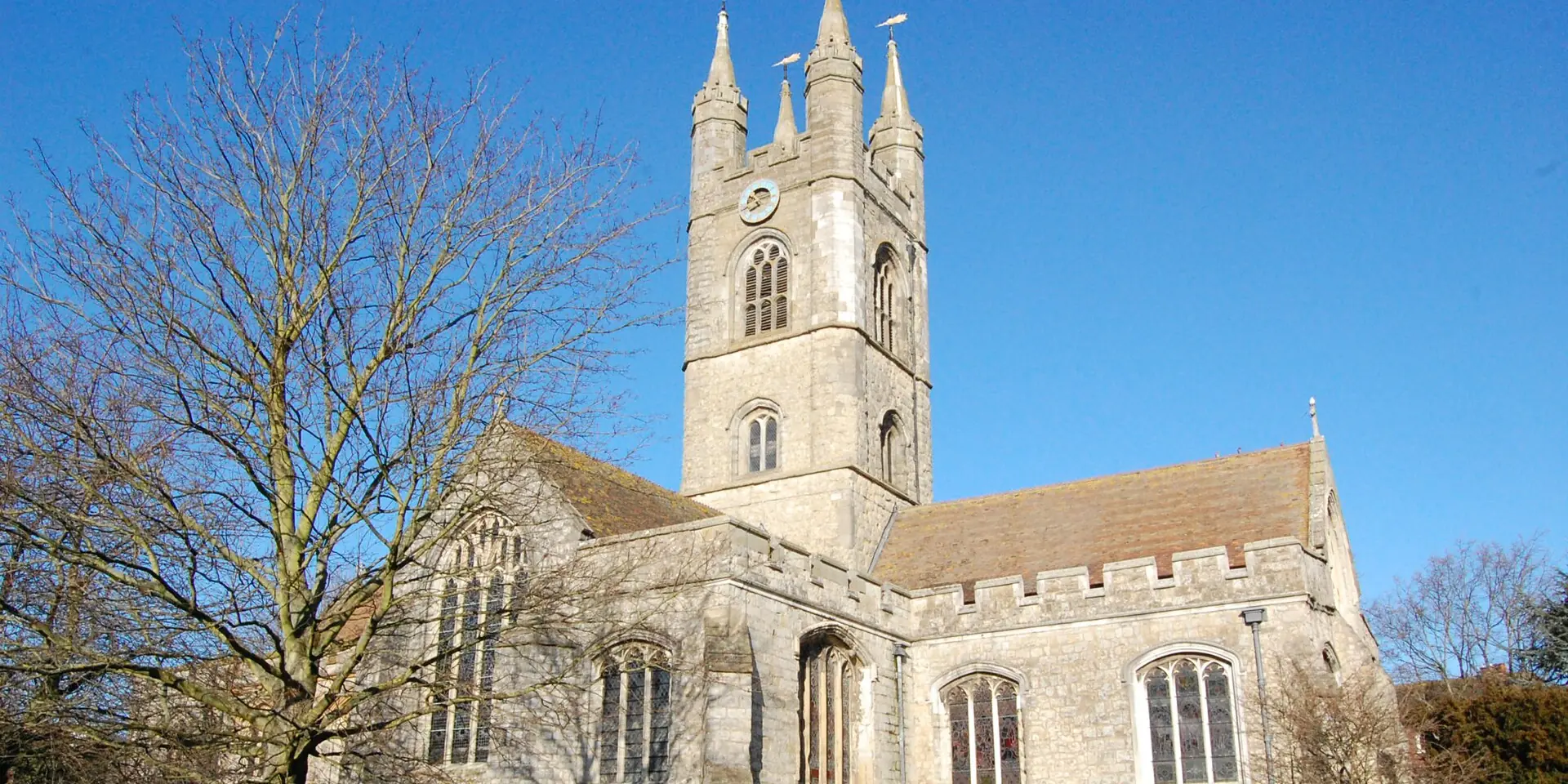 St Mary's Church in Ashford, its pinnacled tower against a clear blue sky above the churchyard