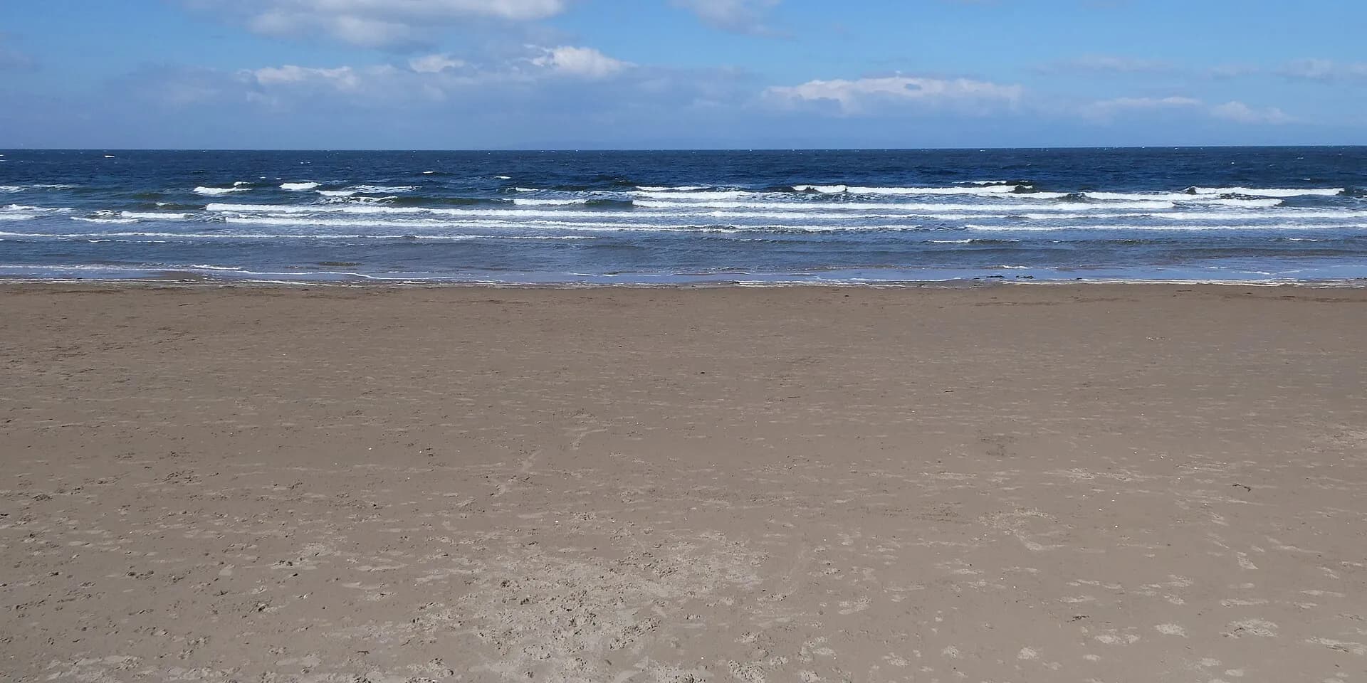 The wide sandy beach at Ayr, with waves rolling in under a blue sky