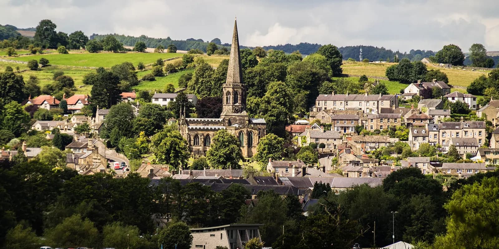 Bakewell's stone houses and church spire among trees, with green Peak District hills behind