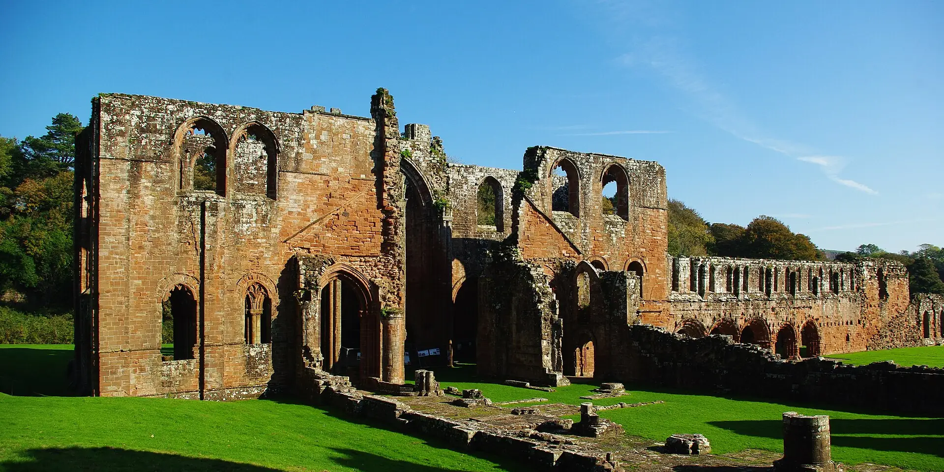 The red sandstone ruins of Furness Abbey on a green lawn under a blue sky