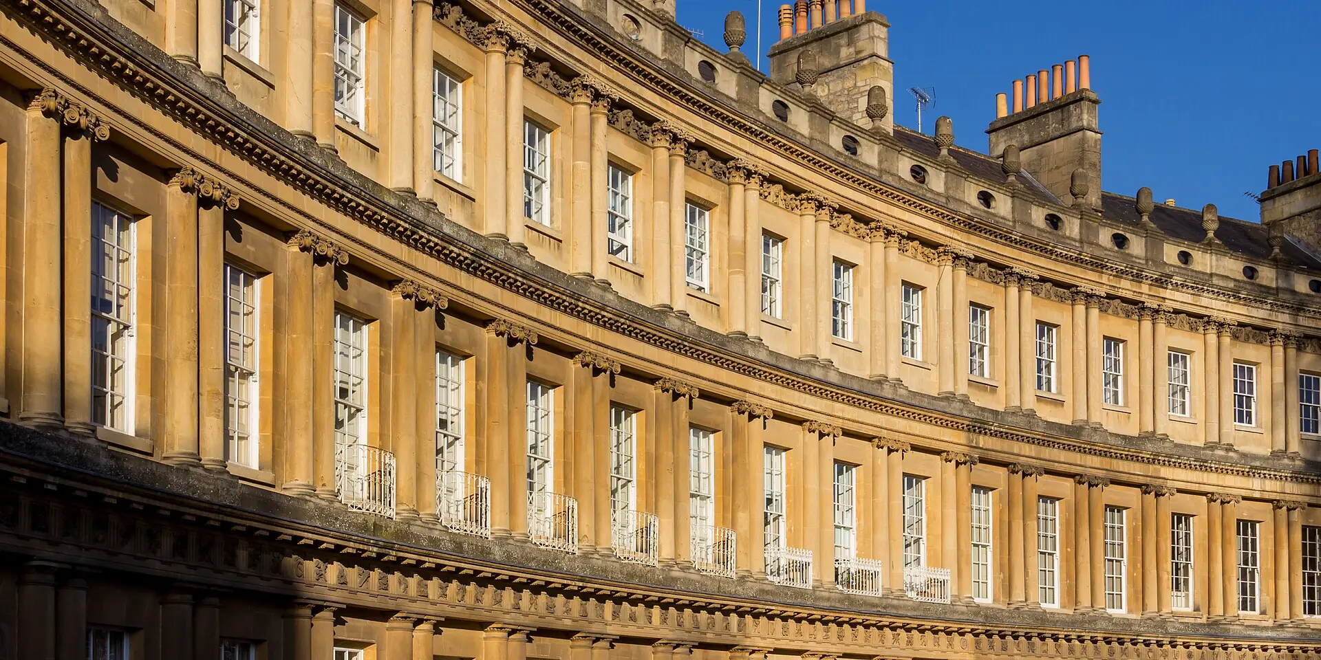 The sweeping golden stone curve of the Royal Crescent in Bath, under a blue sky