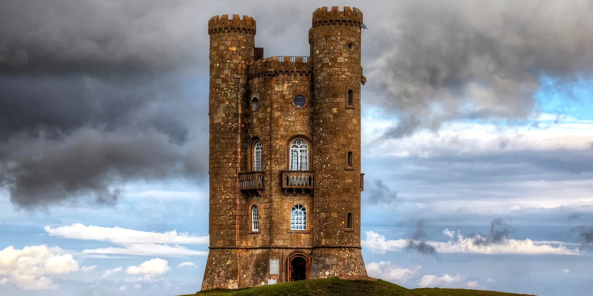 Broadway Tower, a tall stone folly with turrets, standing on a hilltop under dramatic clouds