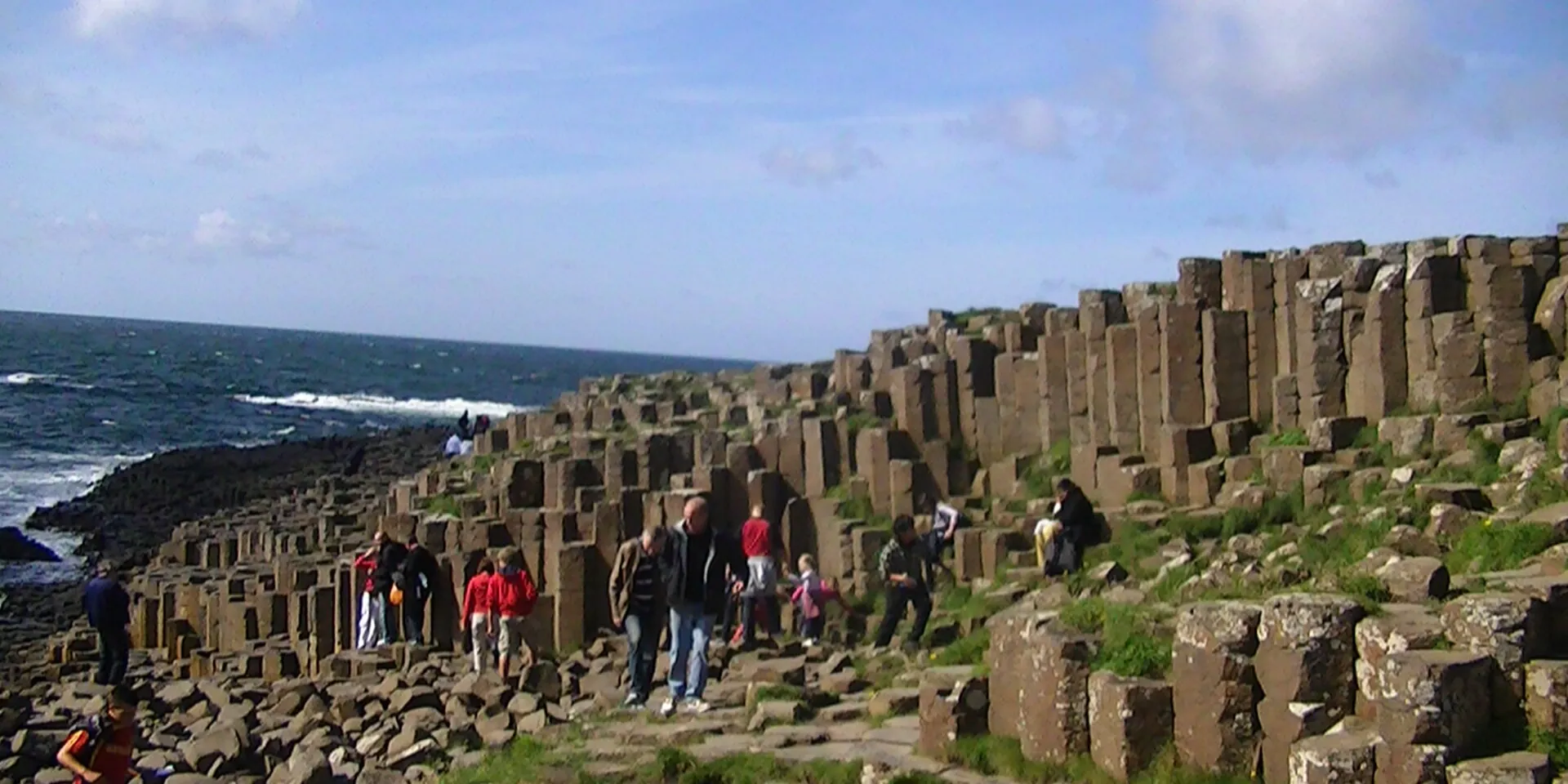 Tall six-sided basalt columns of the Giant's Causeway stepping down to the sea, with walkers on the rocks