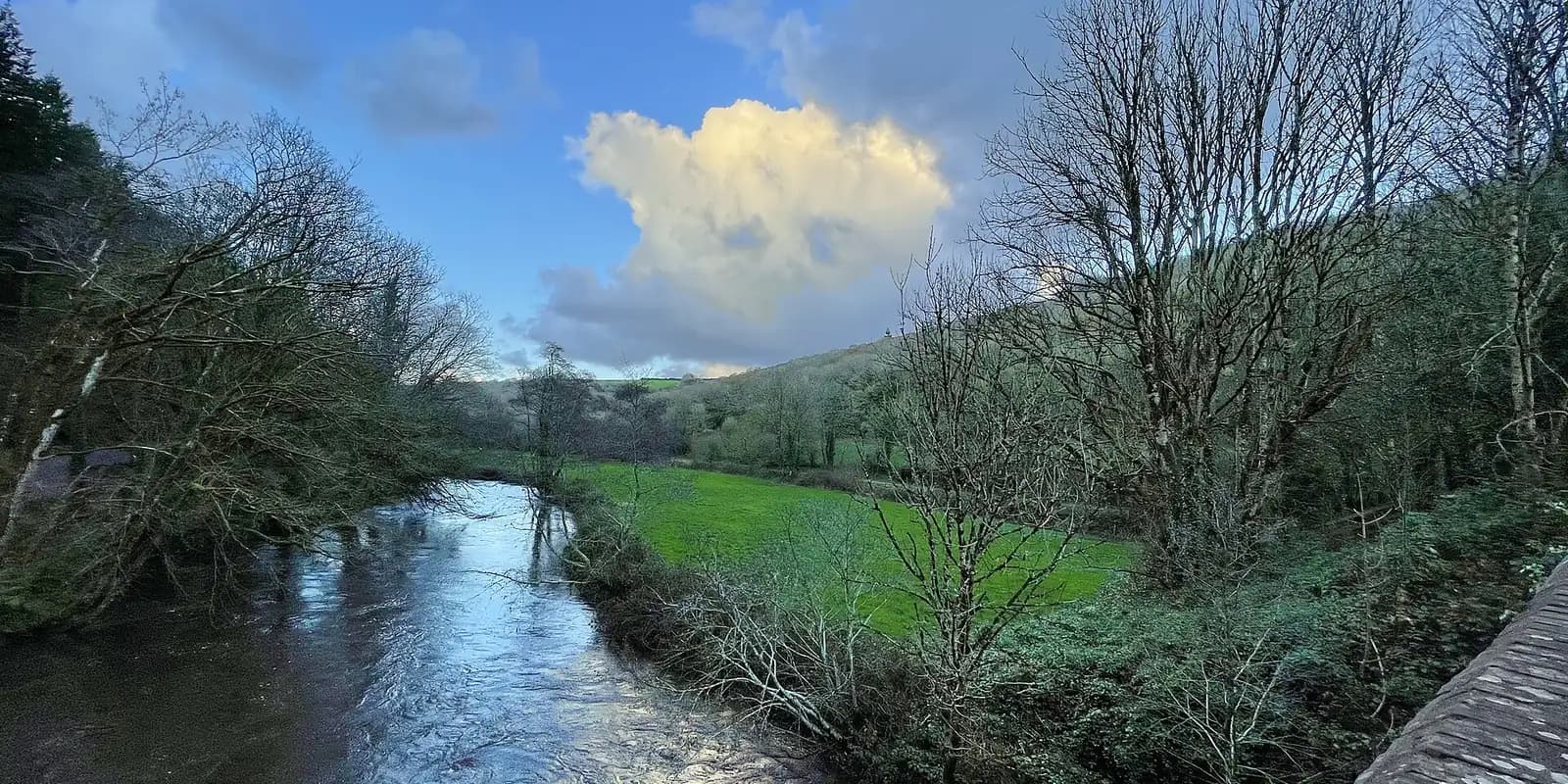The River Camel winding through a green wooded valley under a blue sky