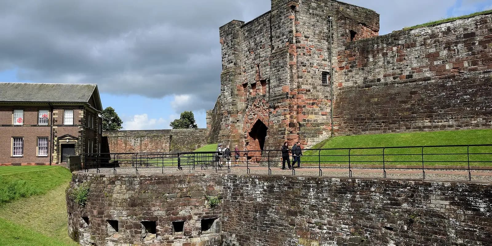 The red sandstone walls and gatehouse of Carlisle Castle above a grassy bank