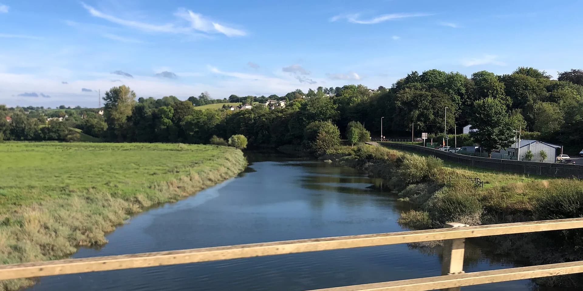 The River Towy flowing between green fields and trees at Carmarthen