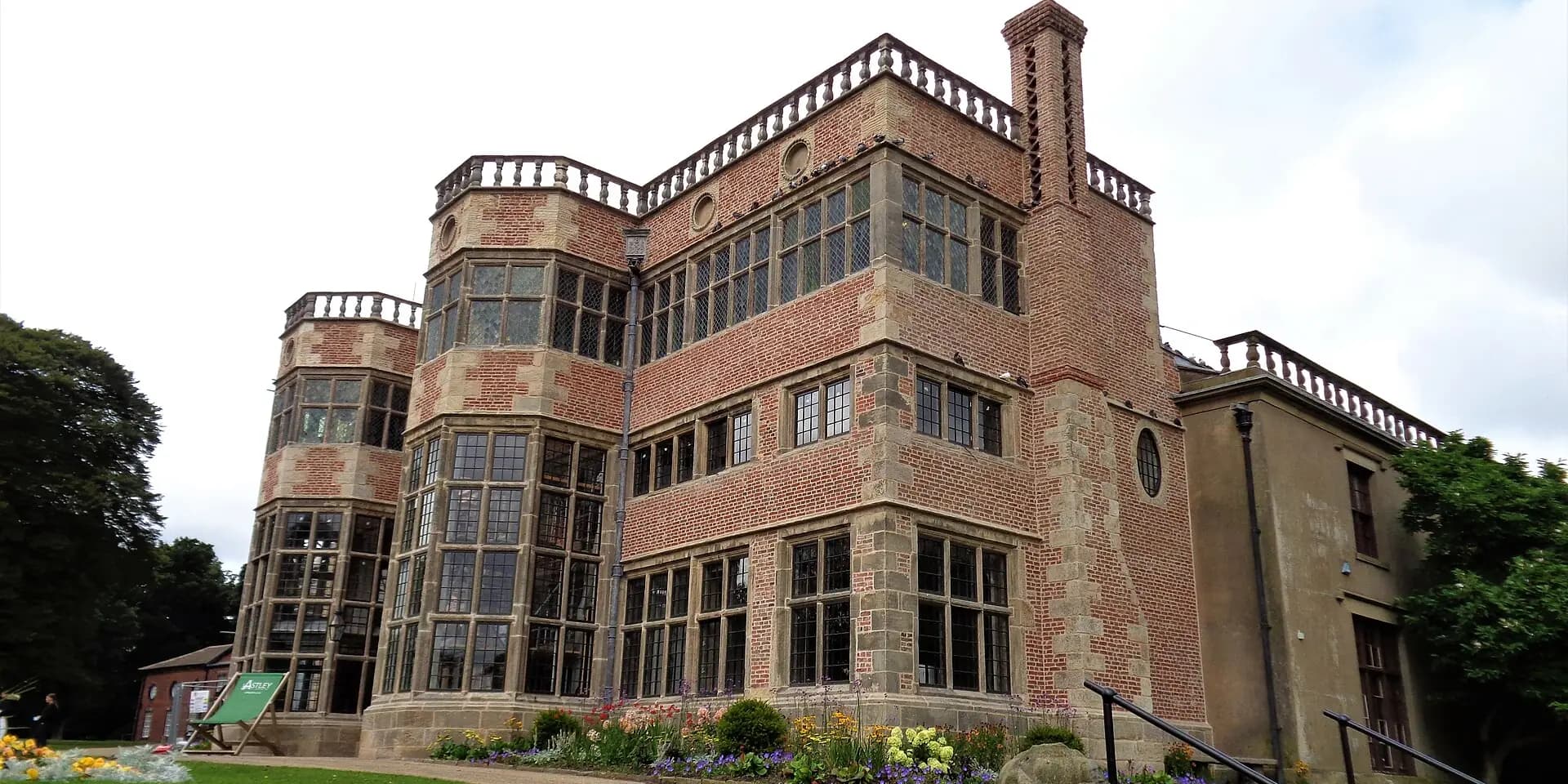 Astley Hall, a red-brick country house with tall bay windows, beside a flower bed