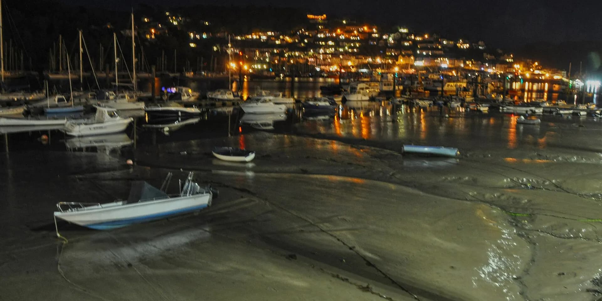 Dartmouth harbour at night, with boats on the water and the lights of the town on the hill across the river