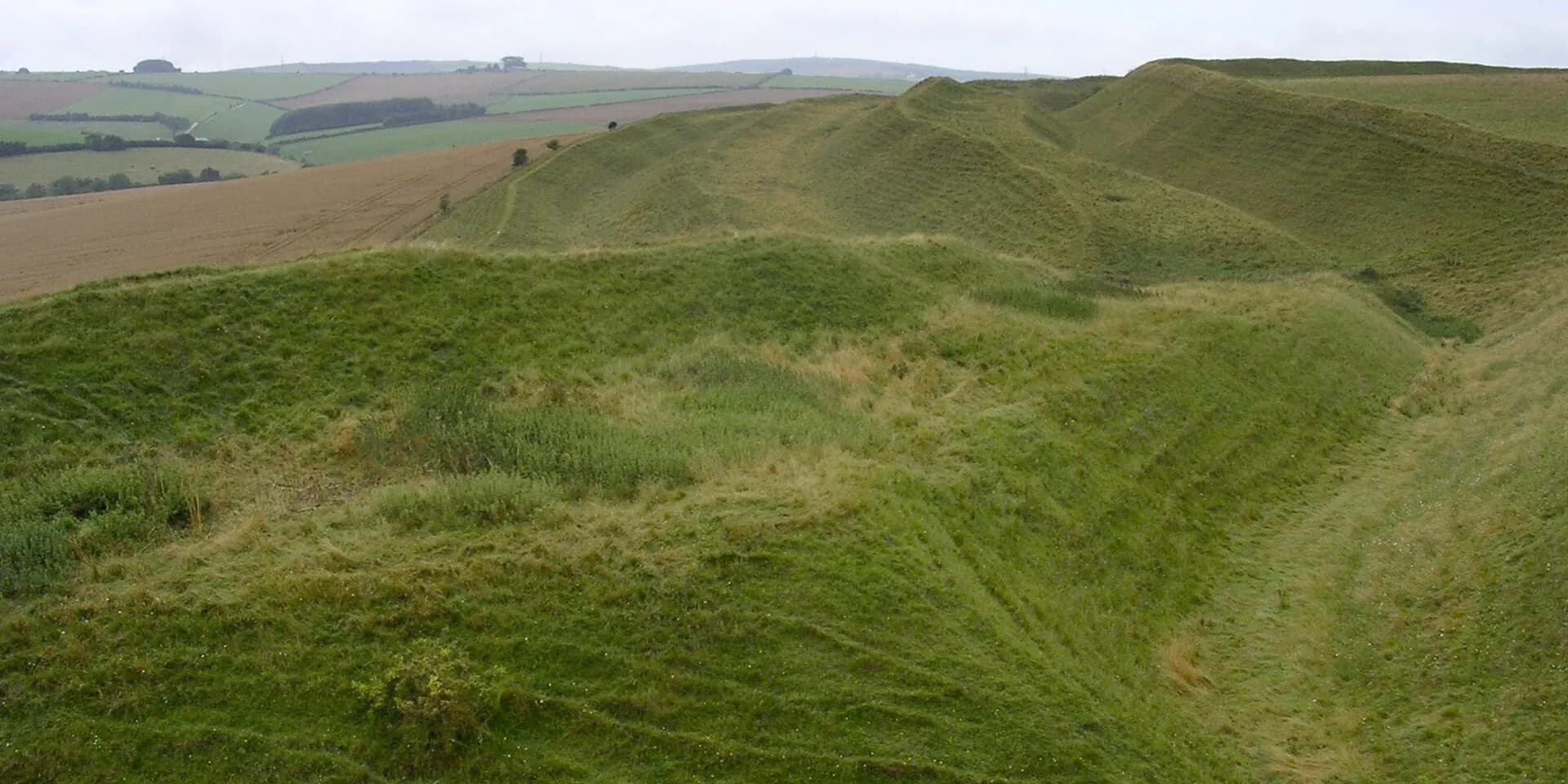 The grassy ramparts and ditches of Maiden Castle hillfort curving away across the Dorset downs