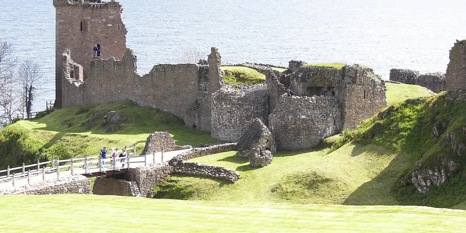 The ruined tower and walls of Urquhart Castle on green slopes beside Loch Ness