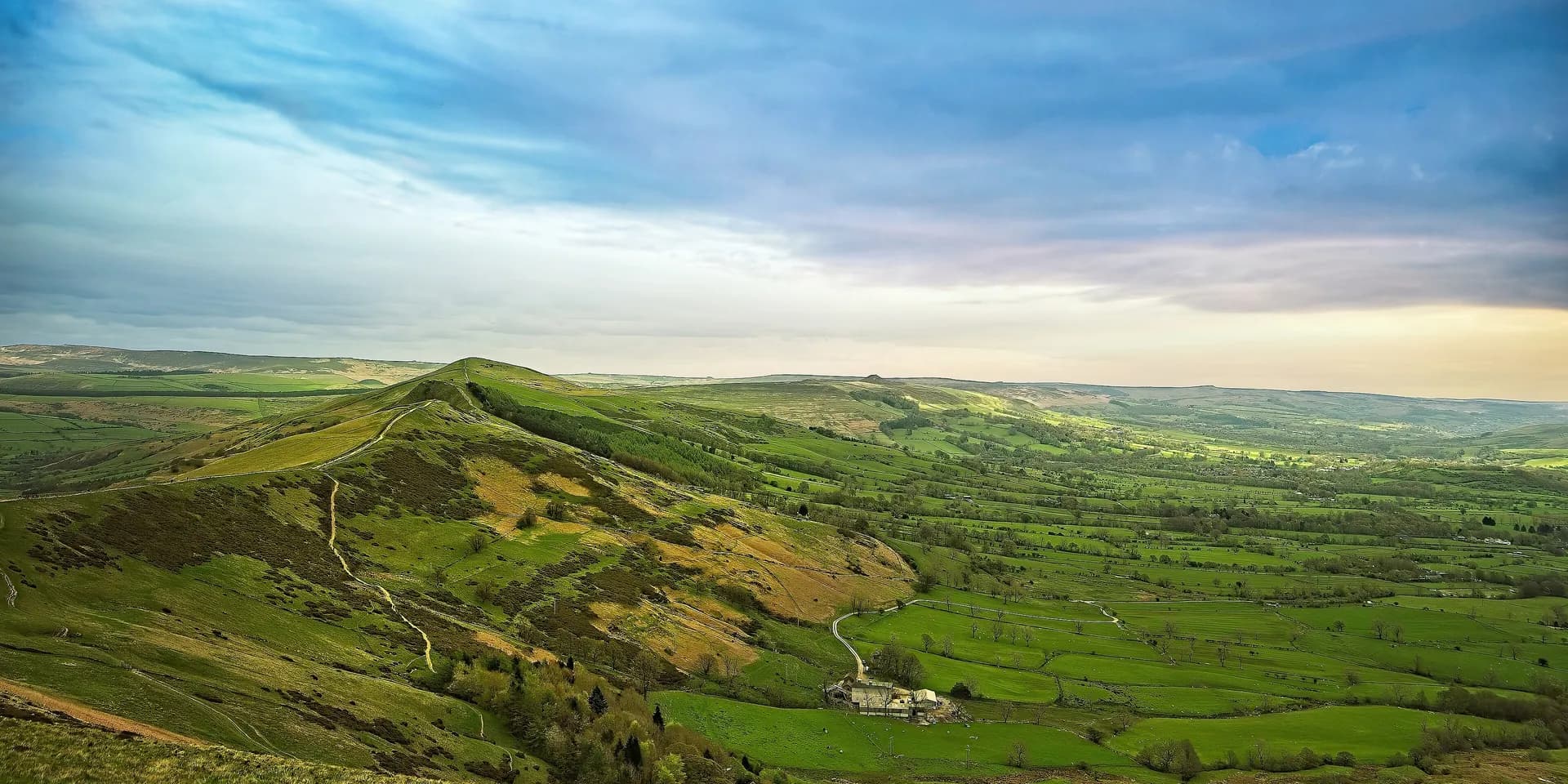 The path along the ridge from Mam Tor, across green hills, with a patchwork of fields in the valley below