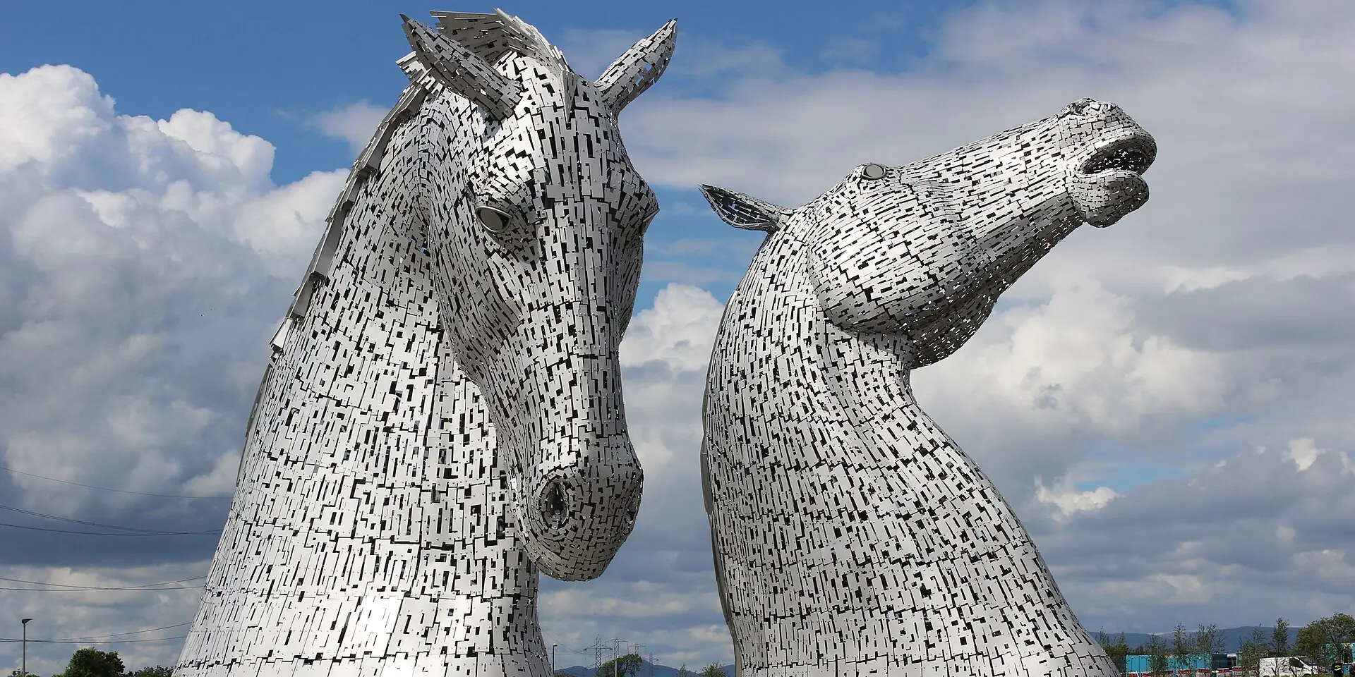 The Kelpies, two giant steel horse-head sculptures, against a blue sky with white clouds