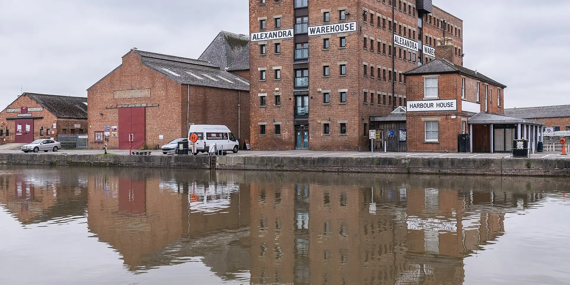 The tall red-brick Alexandra Warehouse reflected in the still water of Gloucester Docks