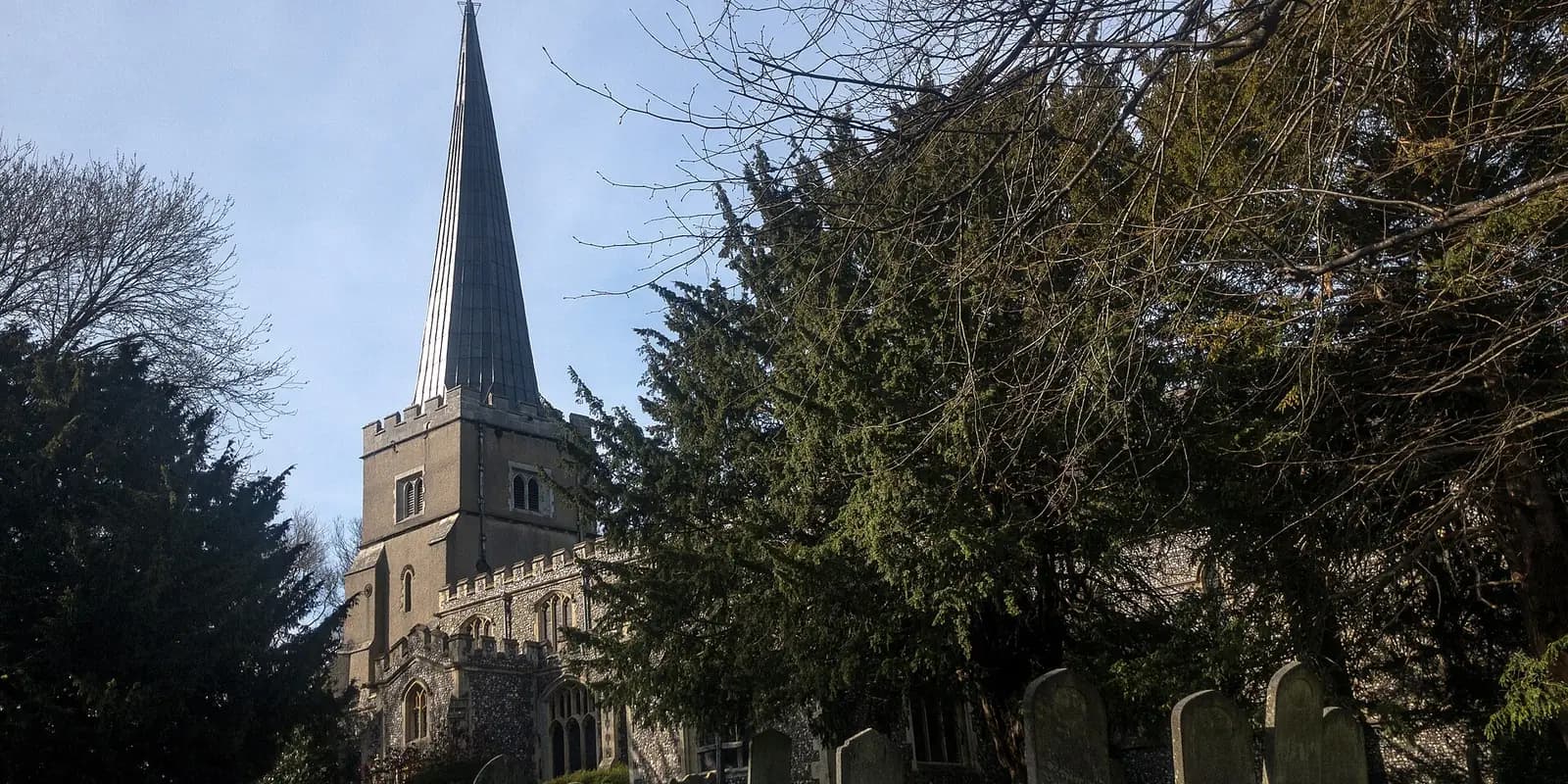 The tall spire of St Mary's Church on Harrow on the Hill, among dark yew trees