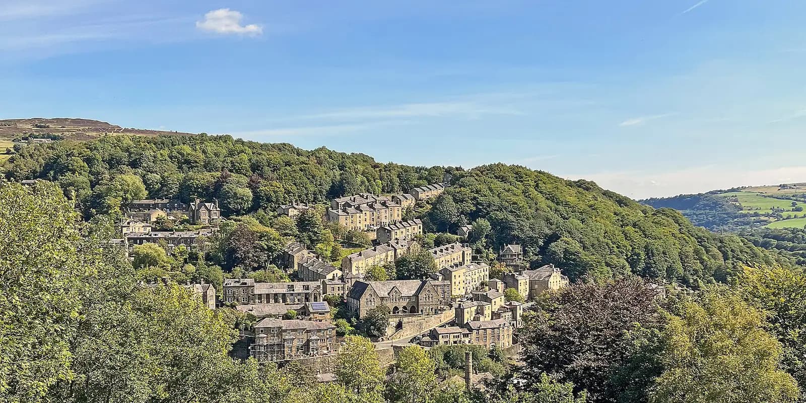 Hebden Bridge's stone terraces stacked up a wooded valley side, under a blue sky