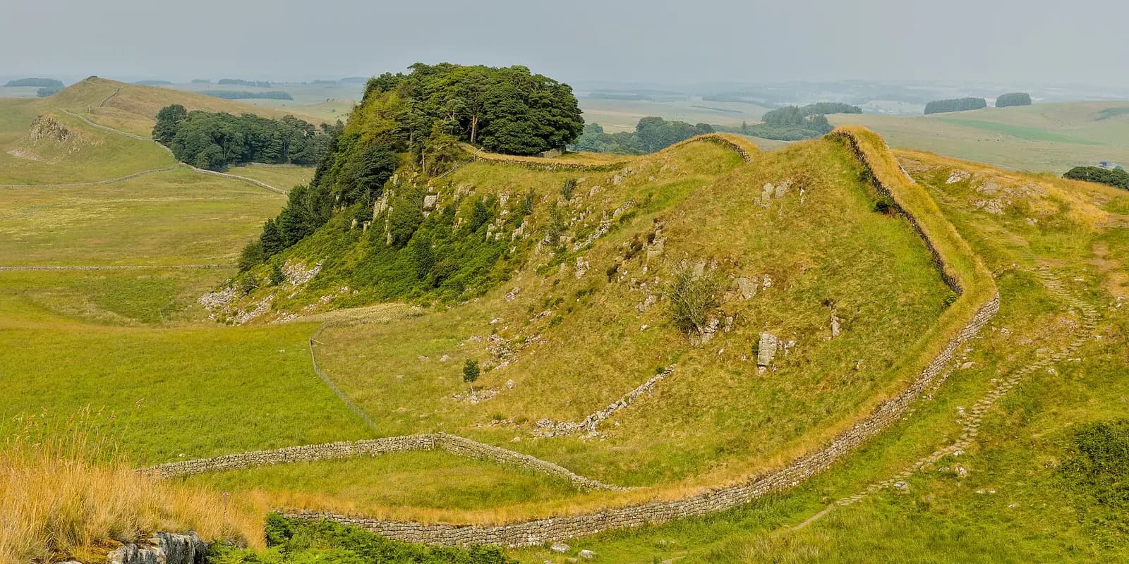 Hadrian's Wall running along a grassy crag above wide open Northumberland countryside