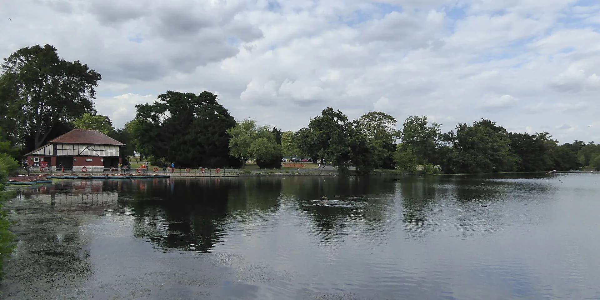 The lake in Valentines Park, Ilford, with trees and a boathouse along the far bank