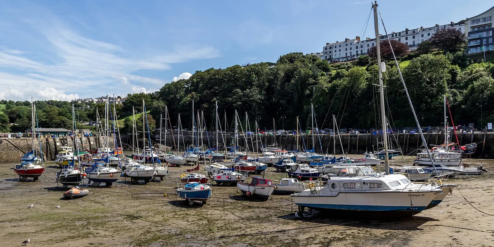 Boats resting on the sand in Ilfracombe harbour at low tide, below wooded hills