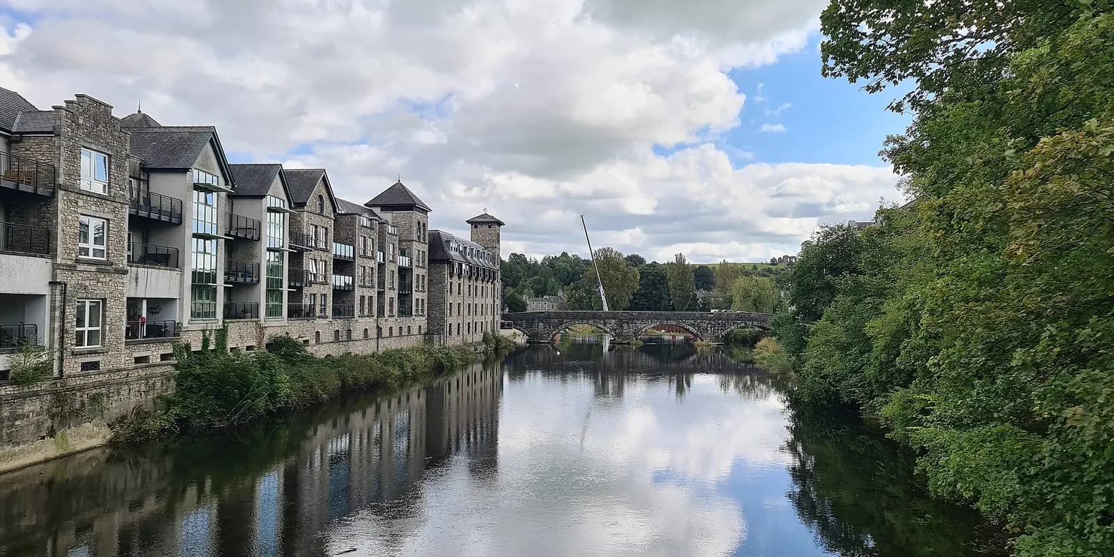 The River Kent flowing through Kendal, with stone buildings and a bridge reflected in the water