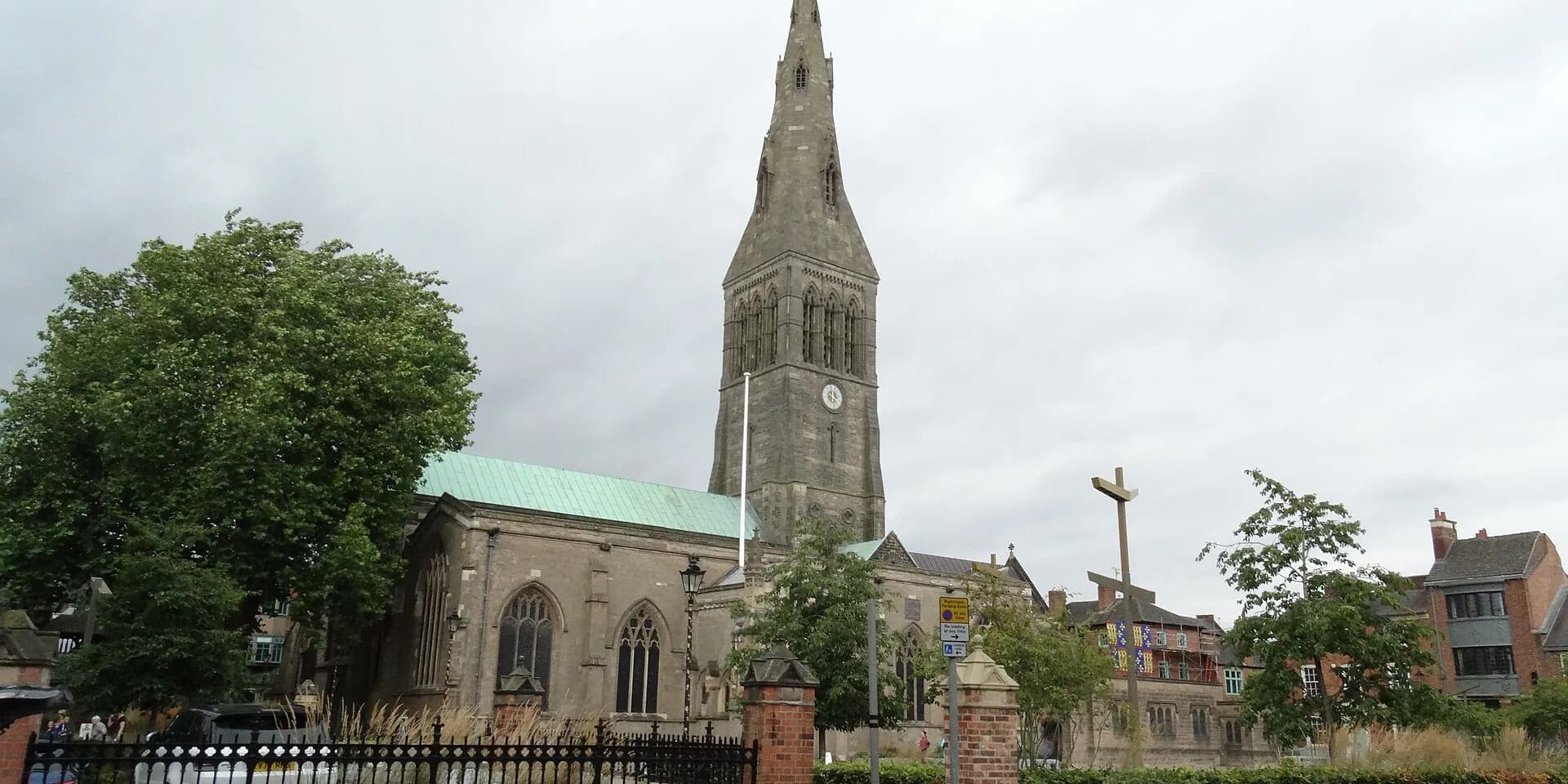 Leicester Cathedral's tall stone spire above trees and the cathedral gardens