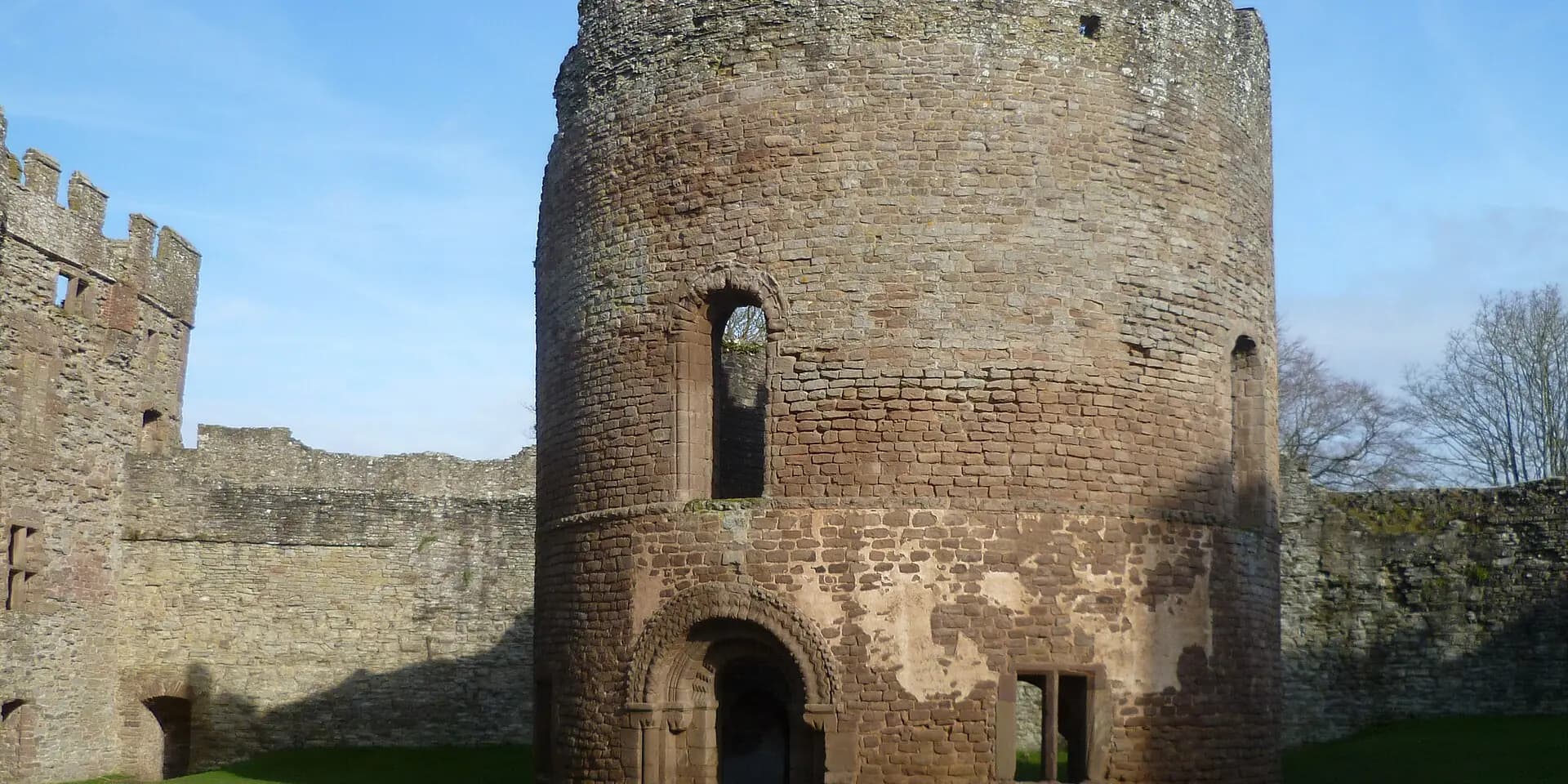 The round Norman chapel and battlemented walls inside Ludlow Castle, under a blue sky