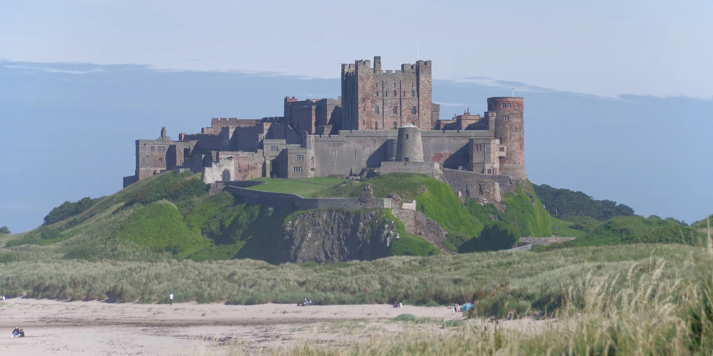Bamburgh Castle on its rocky outcrop above grassy dunes, under a blue sky