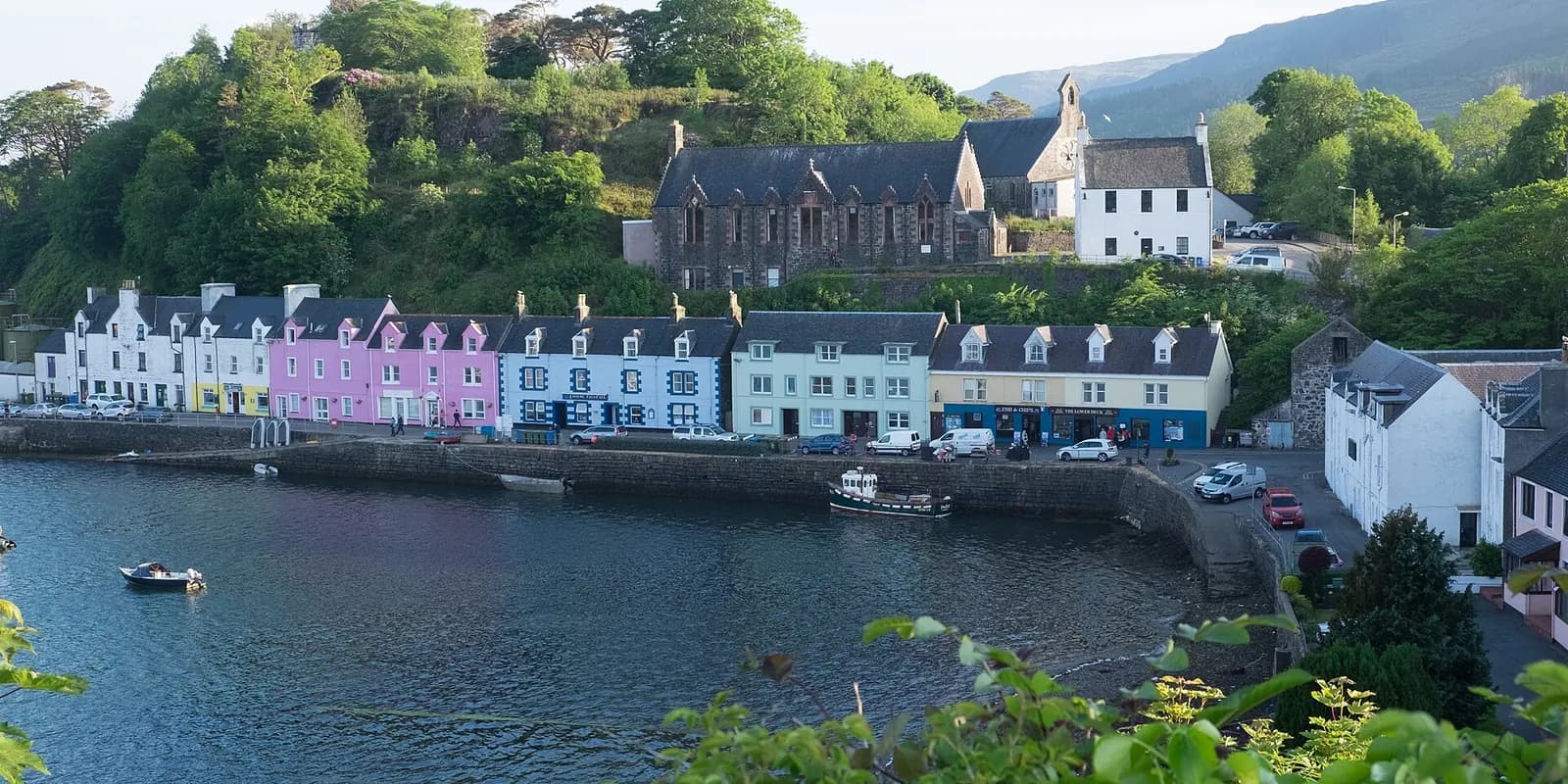 Portree's harbour front, a row of brightly painted houses below wooded slopes