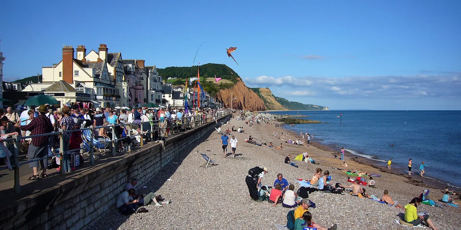Sidmouth's seafront on a sunny day, with people on the beach and red cliffs beyond