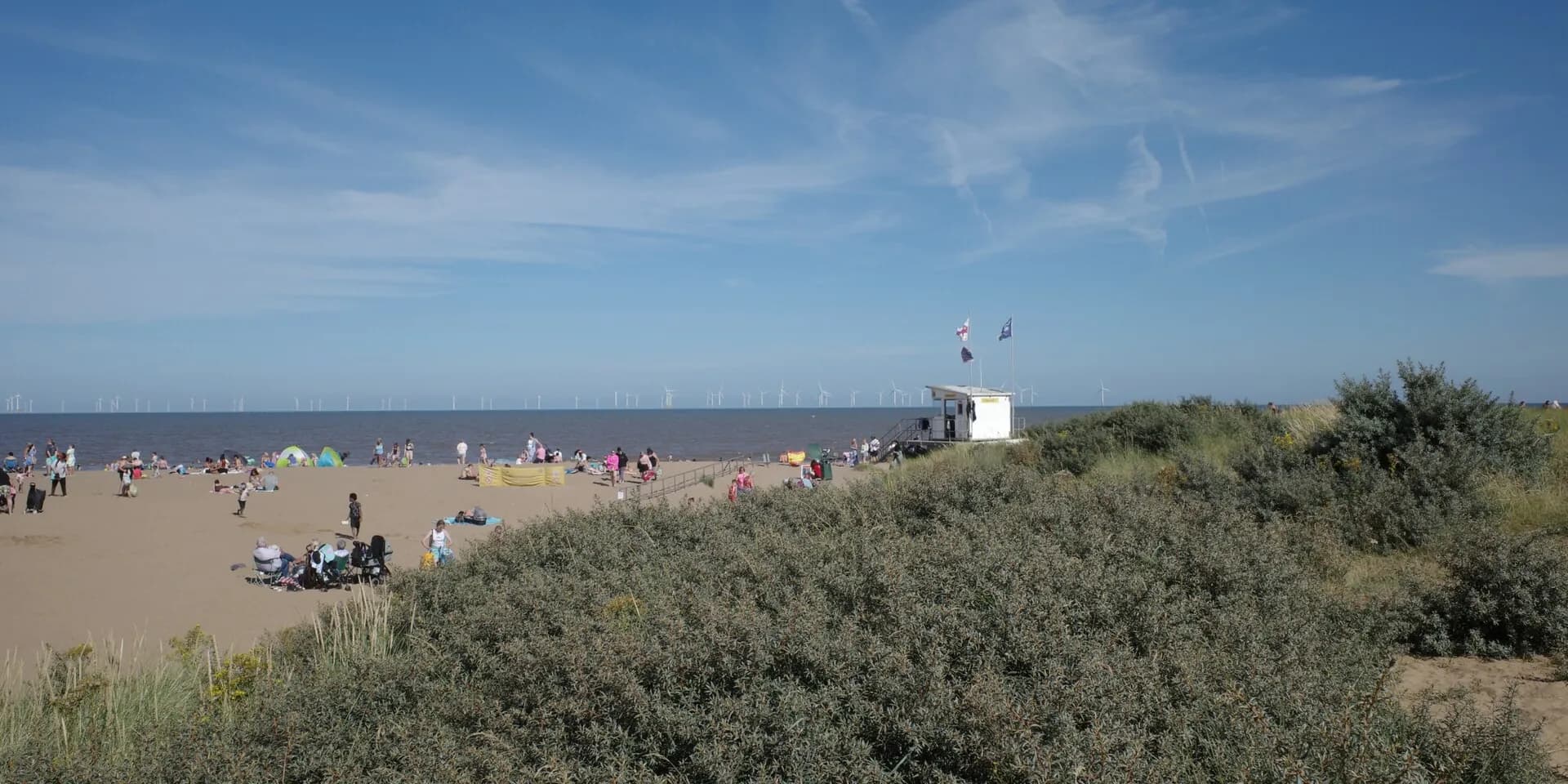Skegness beach on a sunny day, with families on the sand beyond grassy dunes