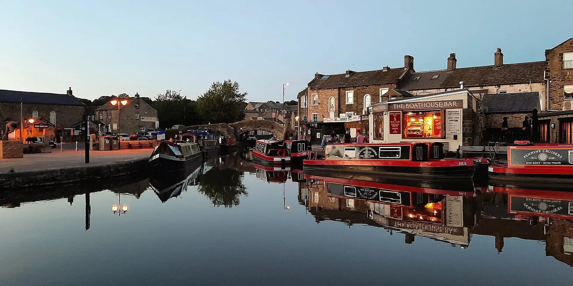 Narrowboats moored in Skipton canal basin at dusk, reflected in still water