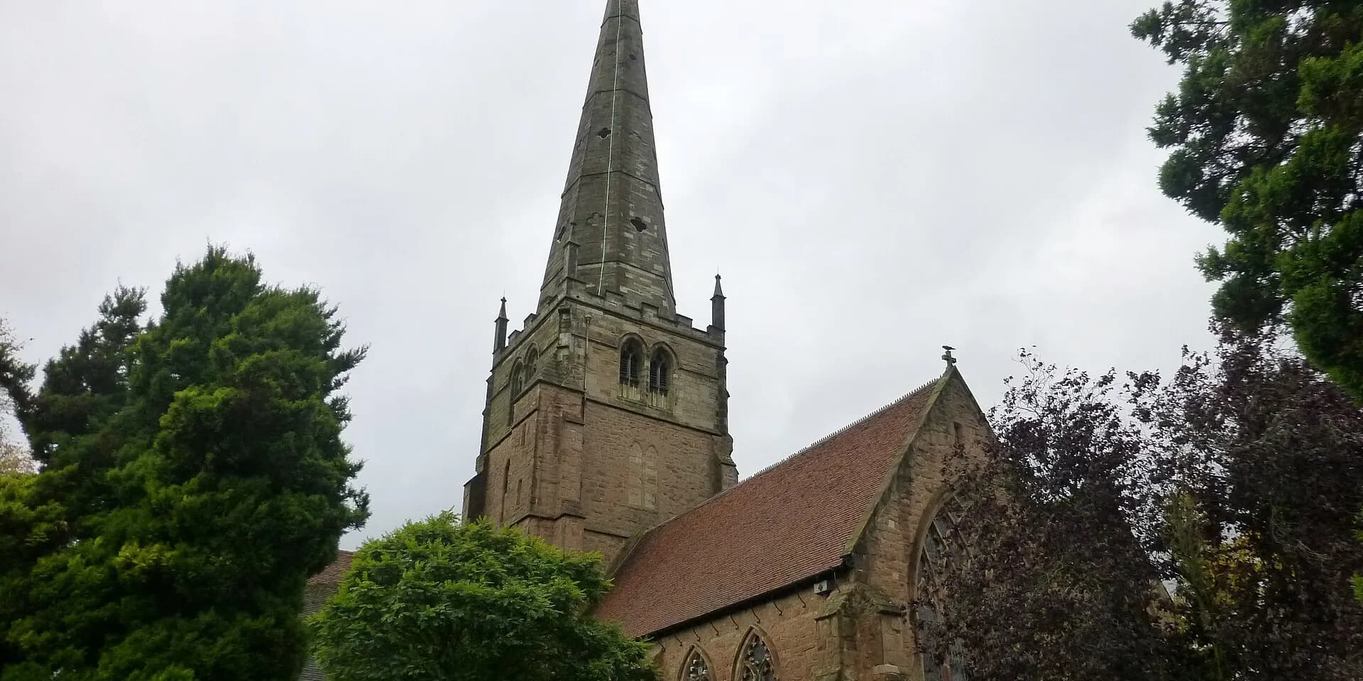 The tall spire of St Alphege's Church in Solihull, among trees