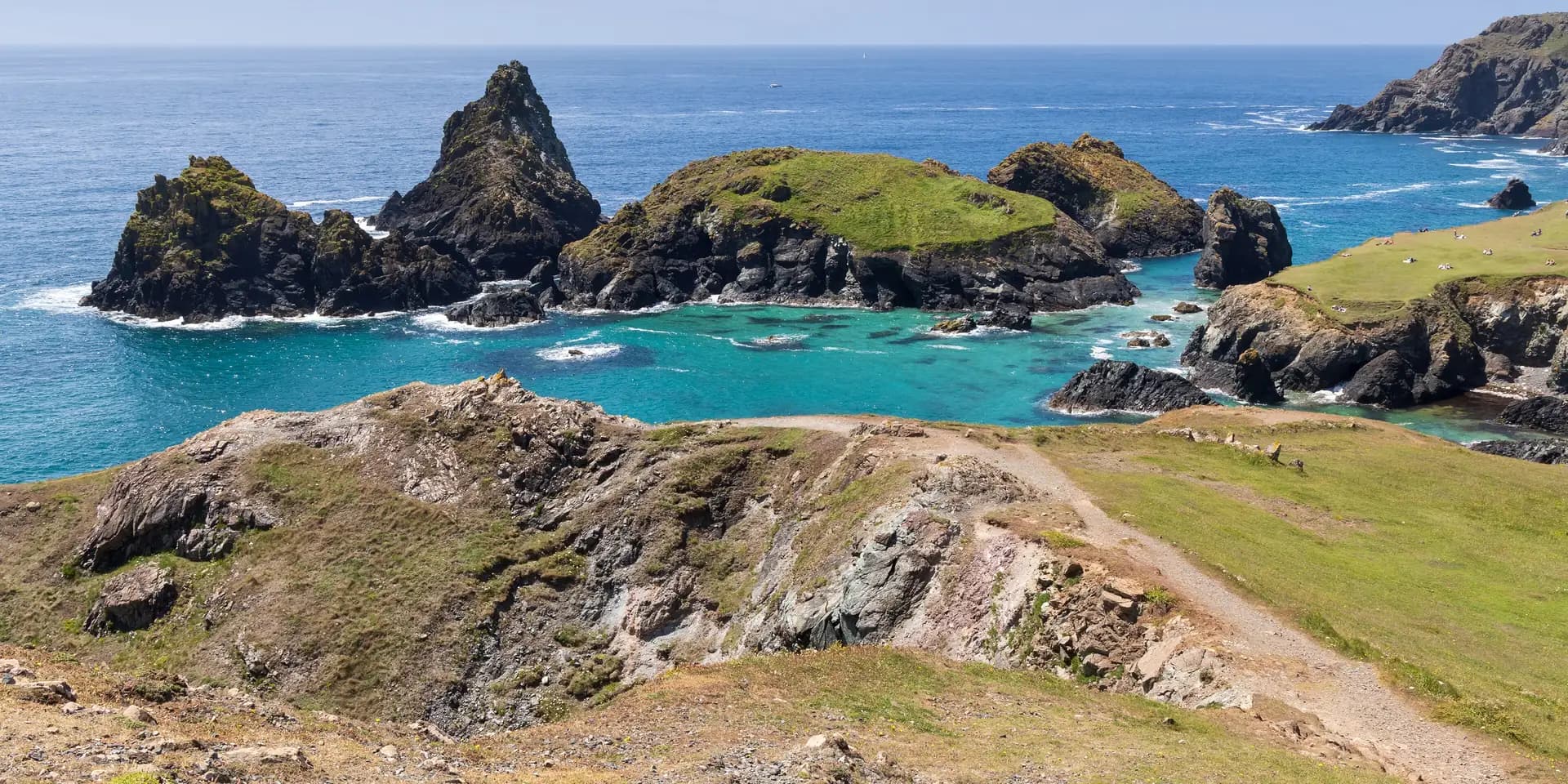 Kynance Cove in Cornwall: turquoise sea around grassy rock stacks, seen from the clifftop path