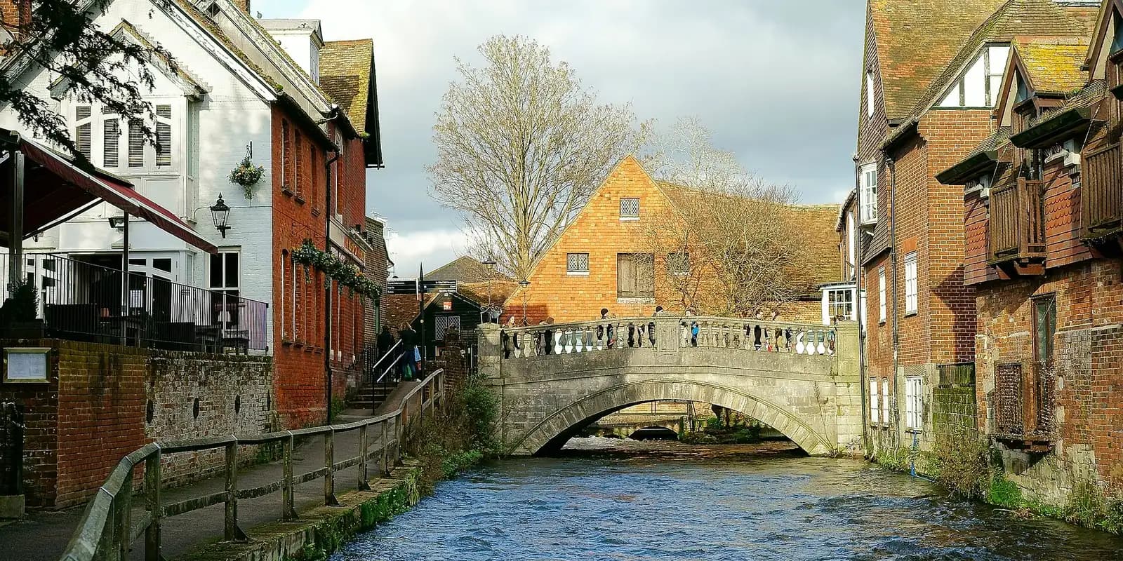 The River Itchen flowing under an old stone bridge between Winchester's buildings
